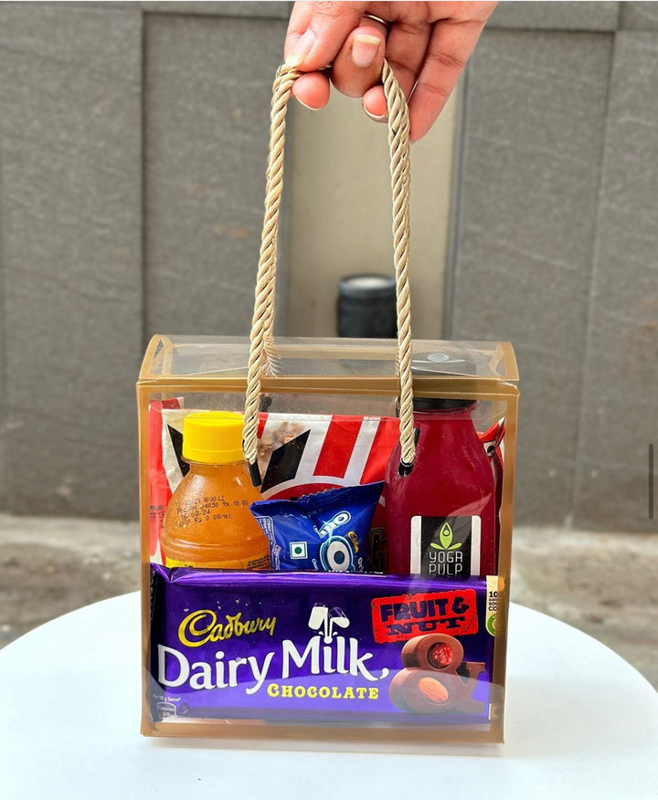 Hand holding a gift basket with Cadbury Dairy Milk chocolate and other items against a neutral background.